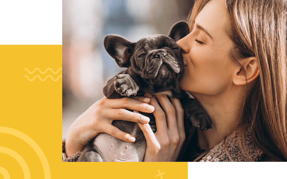 woman holding and kissing a french bulldog puppy